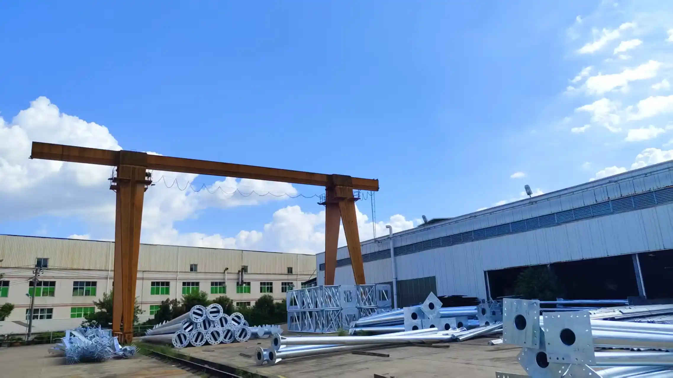Large gantry crane with stacked metal pipes at industrial site​